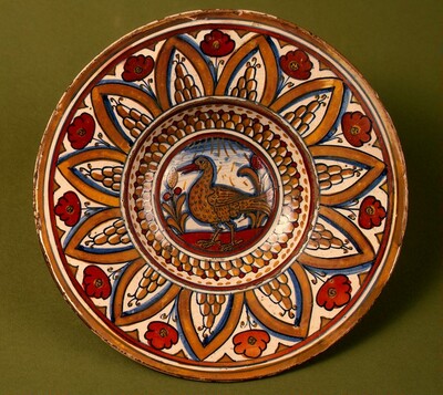 Plate with border of rounded hills within pointed arches with flowers between them; in the center, a wading bird between stylized plants